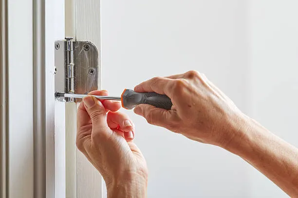 Mãos instalando dobradiça em porta